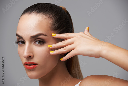 Woman face  beauty and hand with manicure  makeup and yellow nail polish  skin and cosmetics on grey background. Orange lipstick  color nails and model in portrait  confidence in studio and glamour