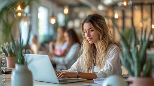 Blonde woman concentrating on laptop in a lively coworking space photo