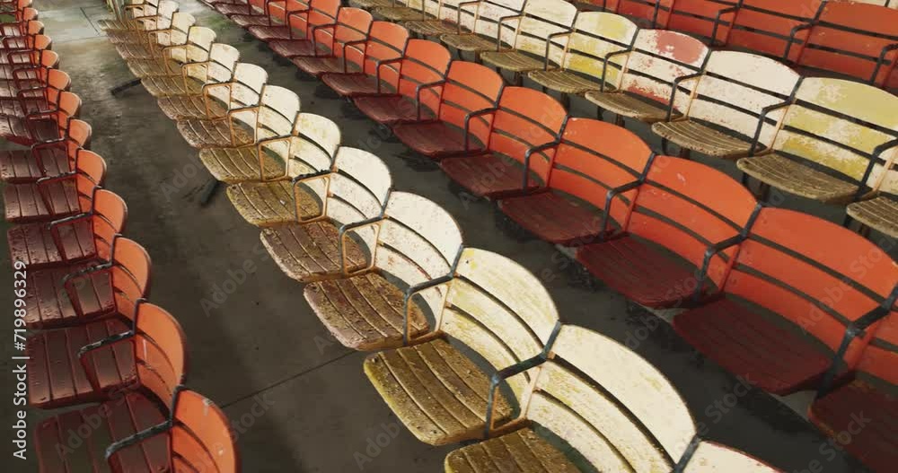 Drone, aerial, video of old faded orange and yellow painted wooden seats at a abandoned a stadium grandstand.
Drone, aerial, video of old faded orange and yellow painted wooden seats at a abandoned a stadium grandstand.