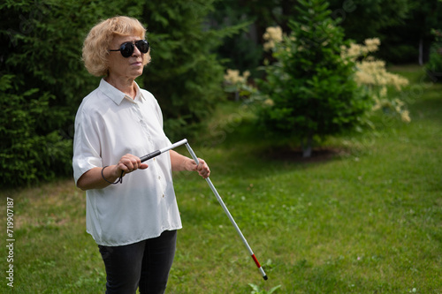 An elderly blind woman lays out a tactile cane while walking in the park.