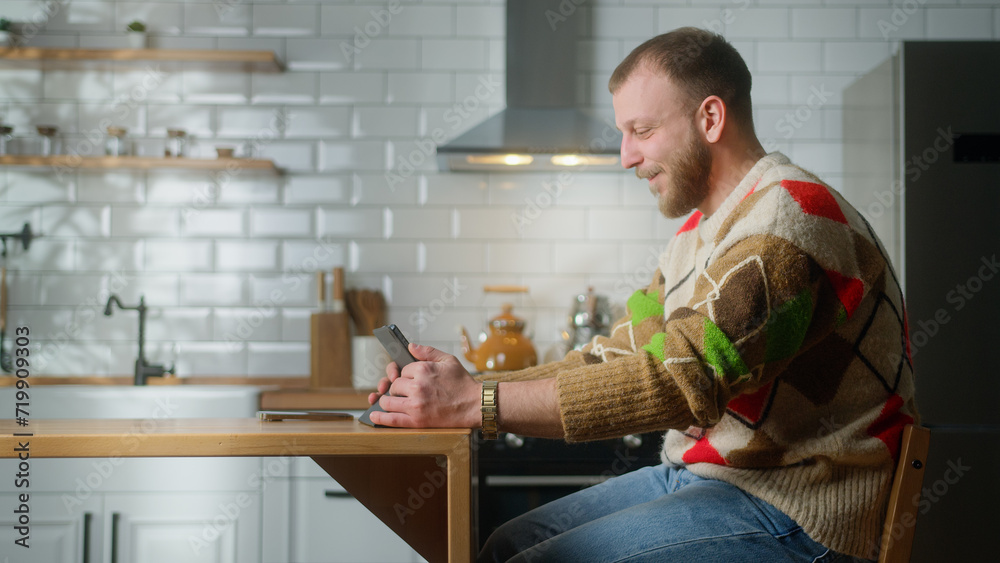 Smiling adult man sitting in the kitchen having video call conversation through tablet device. Share news, talk to family, enjoy web chat virtual meeting. Side shot Smiling adult man sitting in the kitchen having video call conversation through tablet device. Share news, talk to family, enjoy web chat virtual meeting. Side shot