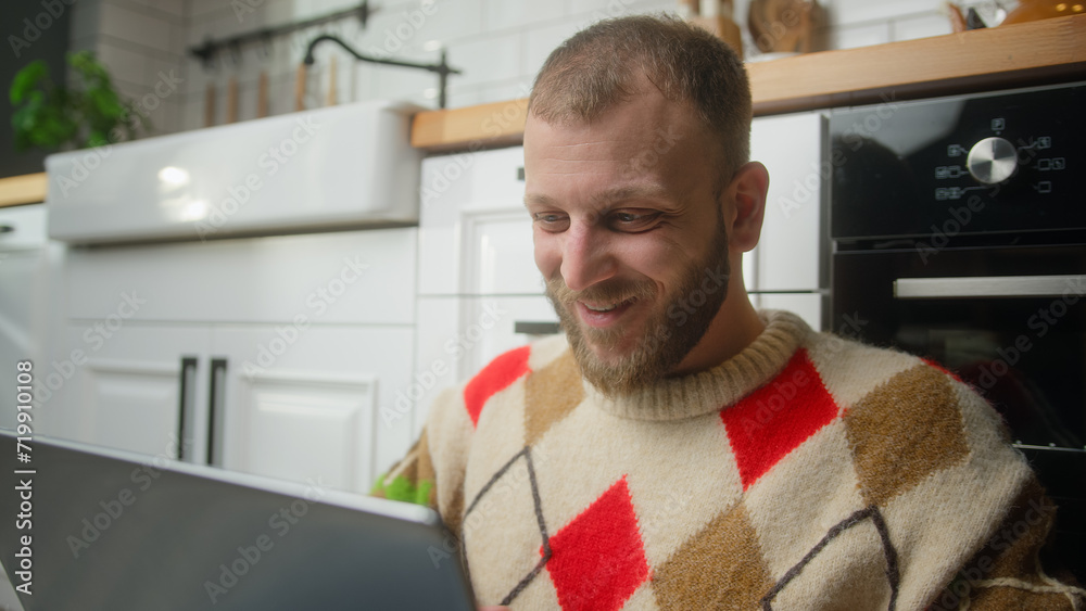 Handsome man sitting on the floor in kitchen typing on laptop enjoying surfing internet, using social media, chatting with friends Handsome man sitting on the floor in kitchen typing on laptop enjoying surfing internet, using social media, chatting with friends