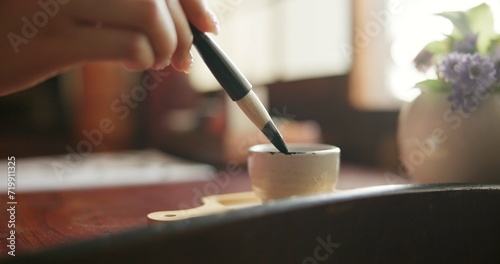 Brush, closeup and hands at a table for calligraphy, writing or ancient Japanese art in a house. Letter, communication and zoom on person fingers with traditional ink stroke, penmanship or art tool photo