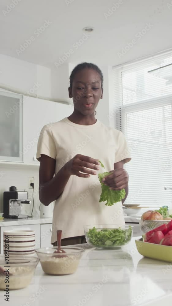 Vertical of black cheerful girl cooking green salad for breakfast or lunch at kitchen Vertical of black cheerful girl cooking green salad for breakfast or lunch at kitchen