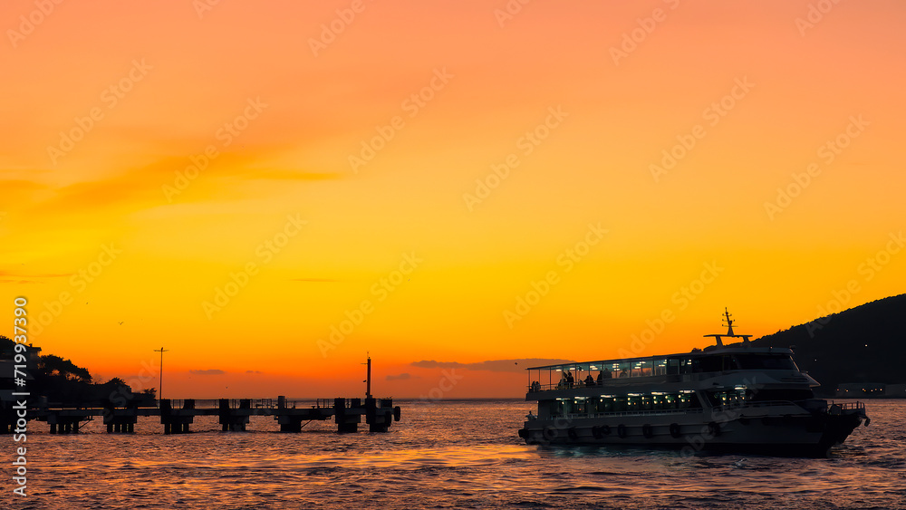 Orange seascape at dawn with silhouettes of passing ferry boat. Turkey
