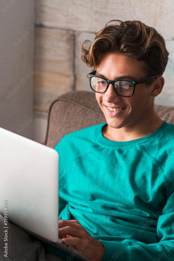 Young caucasian student study at home with internet and laptop computer sitting on the couch - home school concept - video conference and communicating people - happy boy Young caucasian student study at home with internet and laptop computer sitting on the couch - home school concept - video conference and communicating people - happy boy
