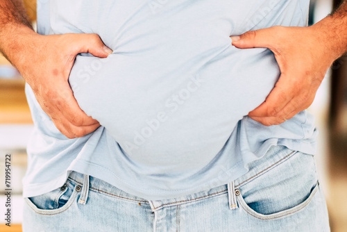 Caucasian fat man hold his belly with hands - diet and healthy lifestyle concept - junk food results - home in background and quarantine coronavirus result photo