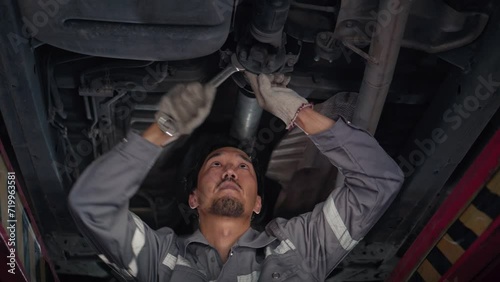 low angle of Japanese auto mechanic working underneath car lifting machine at the garage, asian man worker auto repairs in car service