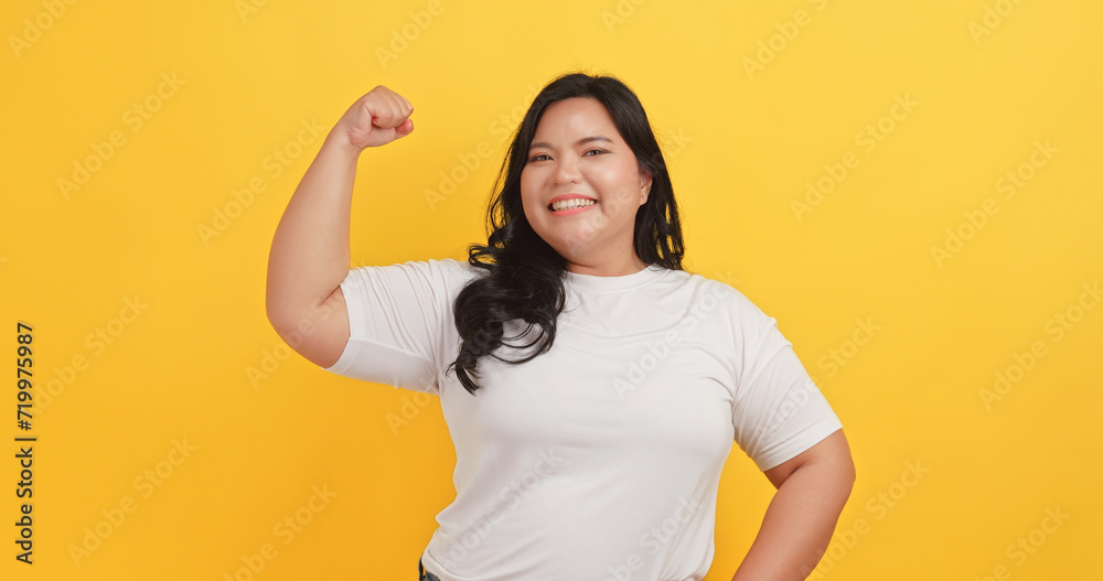 A chubby Asian woman wearing a white t-shirt showing confidence and pride in her appearance on a yellow background. A chubby Asian woman wearing a white t-shirt showing confidence and pride in her appearance on a yellow background.