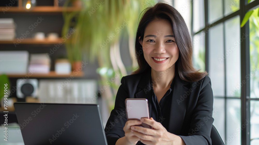 Senior middle aged Asian businesswoman manager ceo using smartphone and laptop in office working online Senior middle aged Asian businesswoman manager ceo using smartphone and laptop in office working online