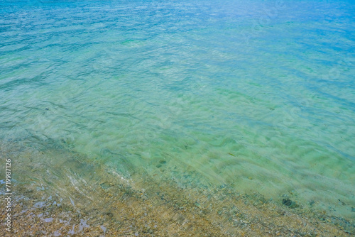Transparent shallow water over sandy beach with visible sea bed.