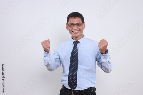 Excited Asian businessman raising both fist showing victory gesture with happy expression