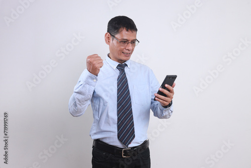 Excited Asian businessman smiling and clenched fist when looking to his mobile phone