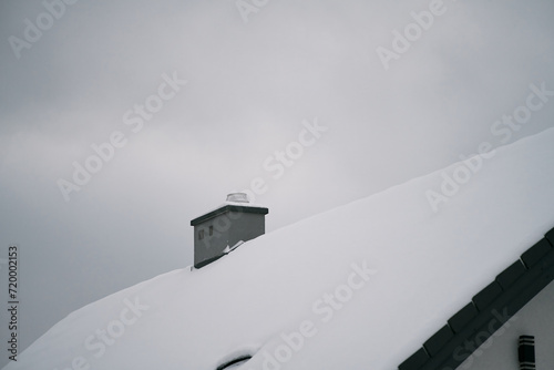 The roof of the family house in winter. Winter landscape with falling snow and the smoke from a chimney heating a home during the chilly season.