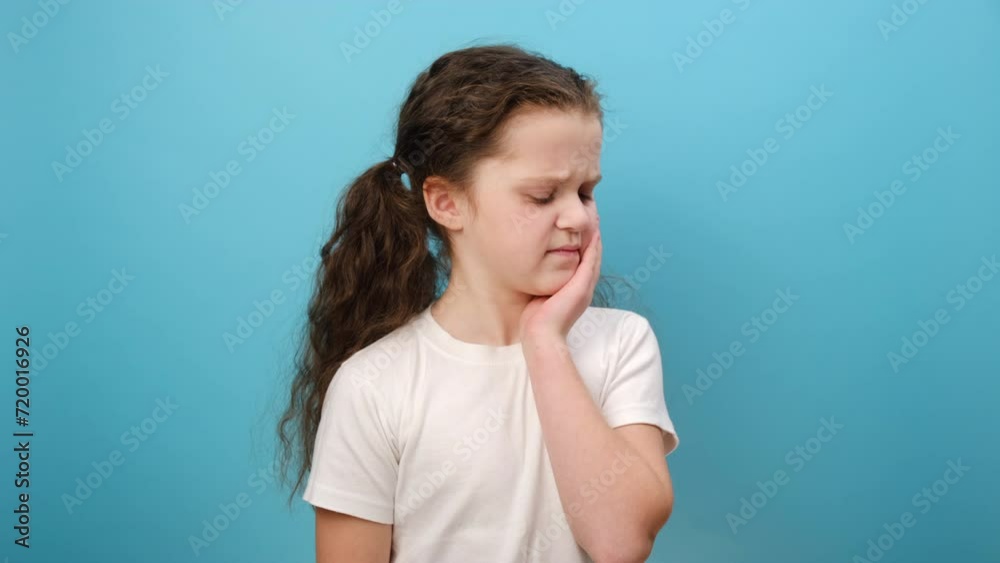 Portrait of sad little girl child suffering from toothache, isolated on blue studio background. Anti toothache remedy. Toothache painkiller. Pain relief concept. Dental disease. Plan to visit dentist Portrait of sad little girl child suffering from toothache, isolated on blue studio background. Anti toothache remedy. Toothache painkiller. Pain relief concept. Dental disease. Plan to visit dentist