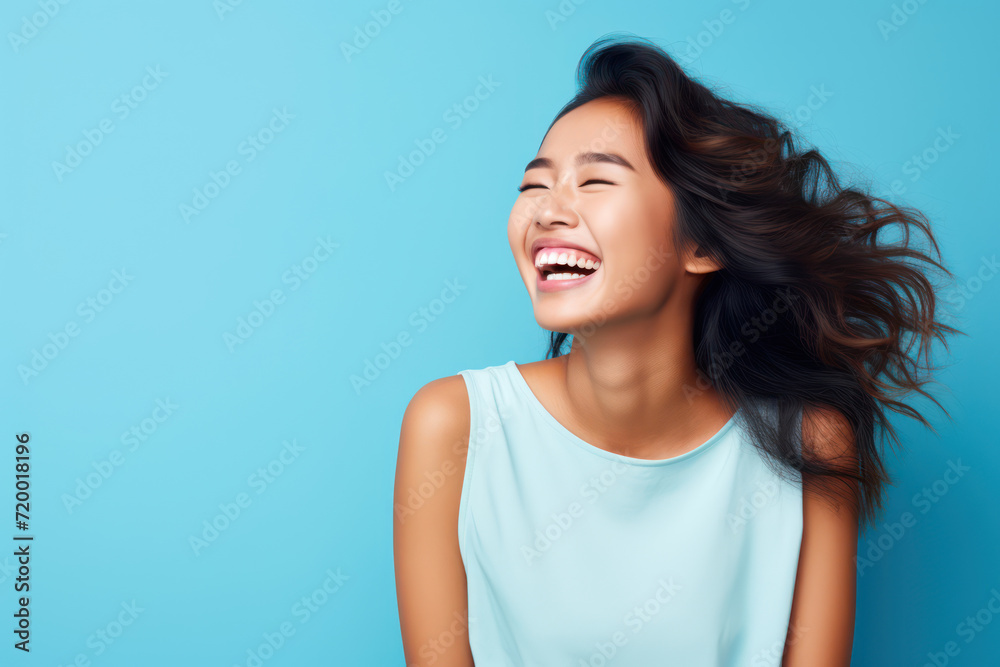 Photograph of a cheerful young Asian woman laughing heartily, with ample copy space on the left, against a light pastel blue background
Photograph of a cheerful young Asian woman laughing heartily, with ample copy space on the left, against a light pastel blue background