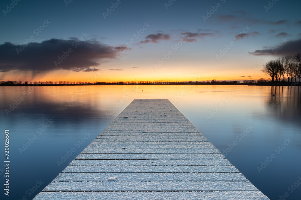 Snow-covered jetty in Lake Dirkshorn with a snow shower on the horizon. The layer of snow that fell during the cold night has remained on the jetty.