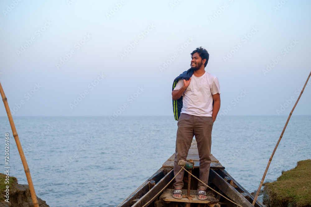Young Bangladeshi traveler sitting on a wooden fishing boat near a river 