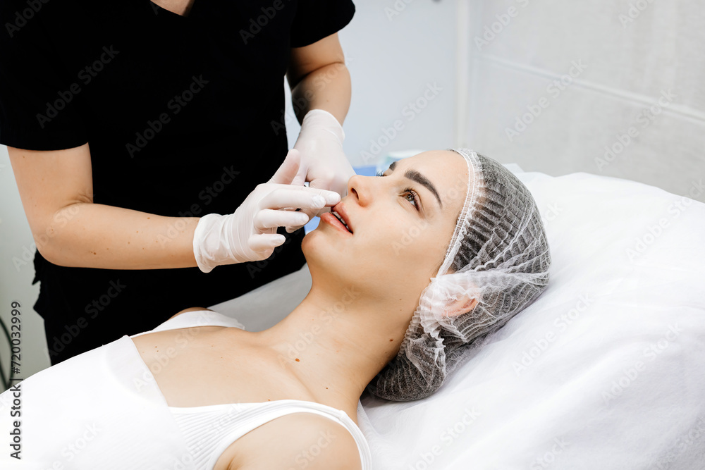 Beauty injections. Lip augmentation procedure. Lip injection. The cosmetologist in medical gloves looks at the result after the injection of the female patient. Beauty injections. Lip augmentation procedure. Lip injection. The cosmetologist in medical gloves looks at the result after the injection of the female patient.