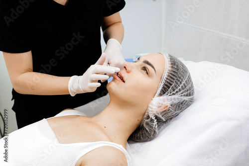 Beauty injections. Lip augmentation procedure. Lip injection. The cosmetologist in medical gloves looks at the result after the injection of the female patient.