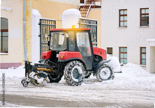 Tractor with sweeper clean snow from sidewalk in downtown. Vehicle with rotating brush and snowplow remove snow from pedestrian zone on road, sidewalk. Snow management during blizzard.