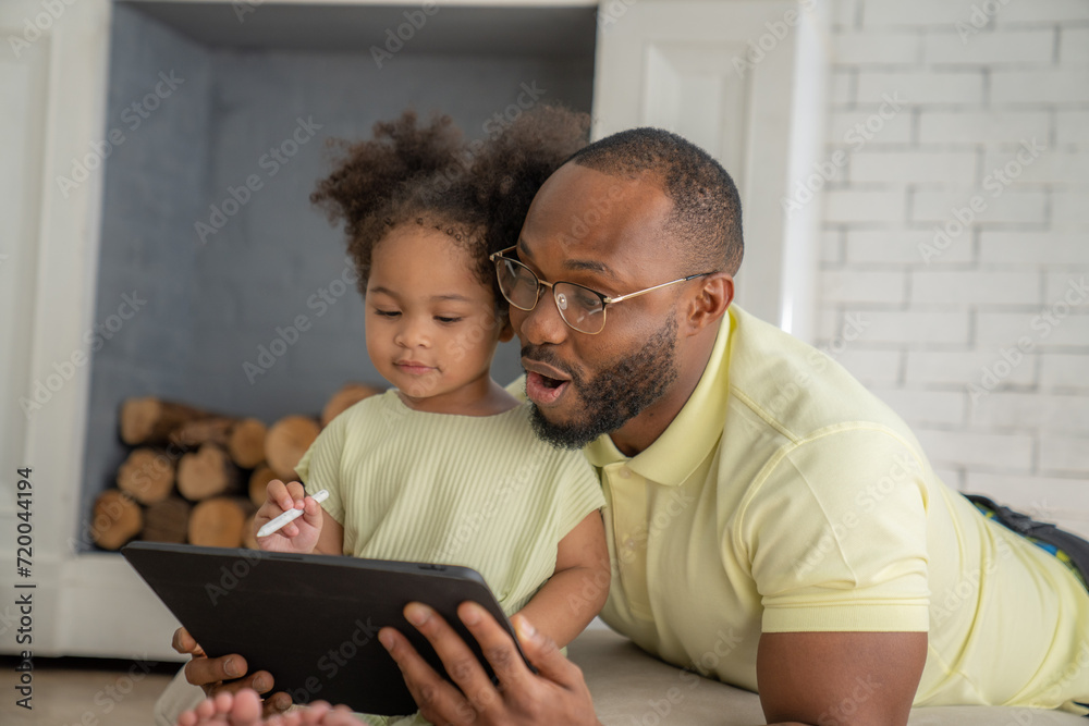 Obraz premium Portrait of African American father and daughter using laptop watching video, smiling while sitting at home.