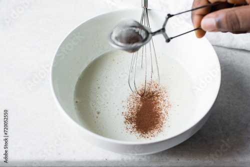 a silver strainer with Cocoa powder, sieving clumpy cocoa powder into batter
