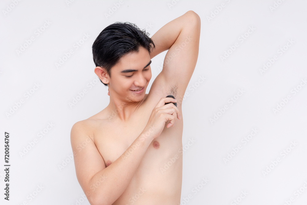Fototapeta premium A man applies roll-on deodorant to his underarms after a bath. Body hygiene and odor prevention. Isolated on a white backdrop.
