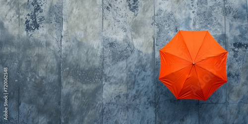 Striking solitary orange umbrella on a wet concrete surface, offering a vibrant splash of color against a monochromatic urban setting