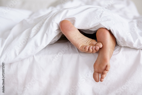 Bed, feet and person sleeping in home, relax and resting nap in sheets for health, calm and leisure in the morning. Foot, bedroom and closeup of toes in blanket, skin of legs and comfort in house © Cameron Mcdonald/peopleimages.com