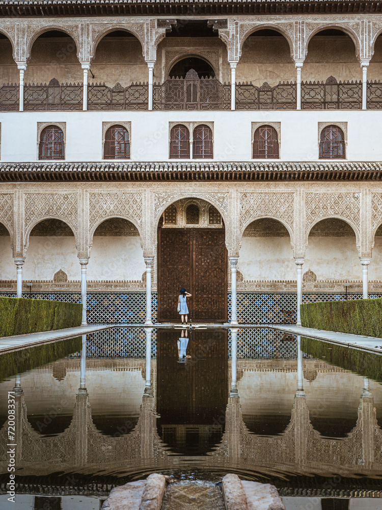 A beautiful young woman female tourist standing in front of the Alhambra door in a blue dress and hat