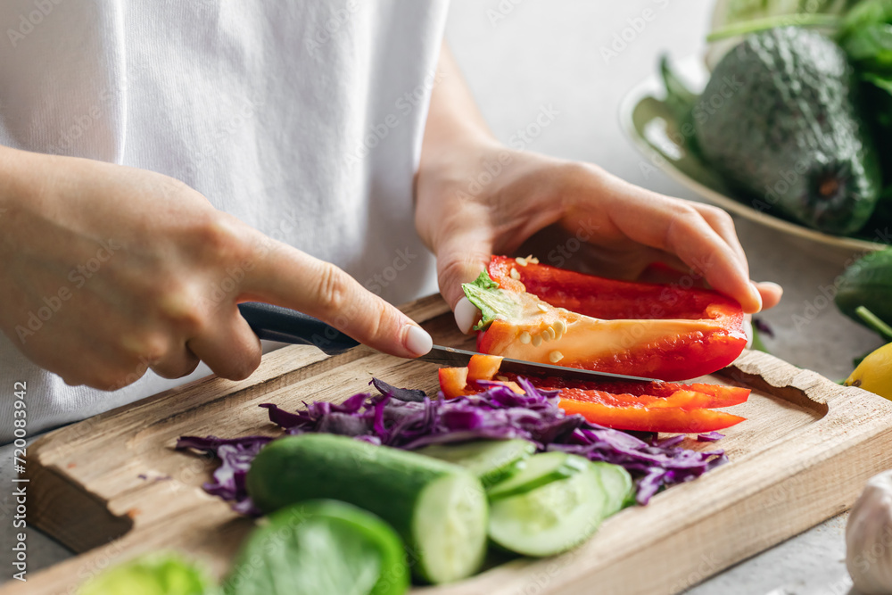 A woman cuts a fresh bell pepper on a wooden board in the kitchen. A woman cuts a fresh bell pepper on a wooden board in the kitchen.