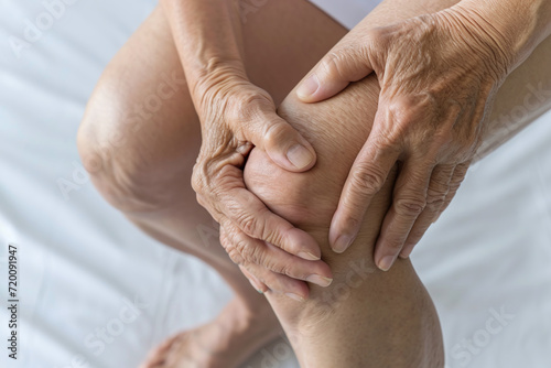 An elderly woman holds on to her sore knee with arthrosis, sharp pain in her leg photo