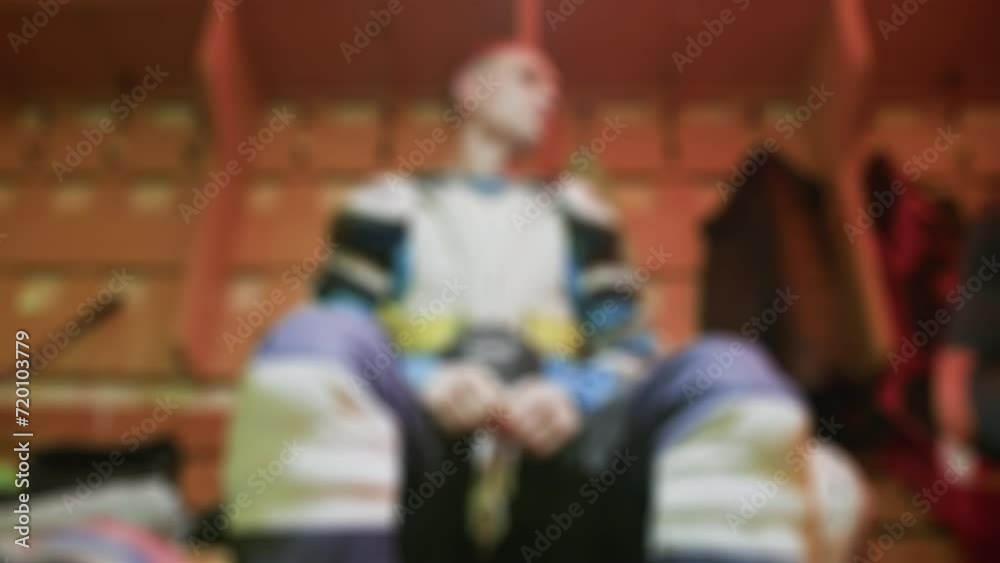 Ice hockey player dressed in protective gear without a jersey and helmet sits in the locker room before the start of a game. Cloakroom inside. Blurred