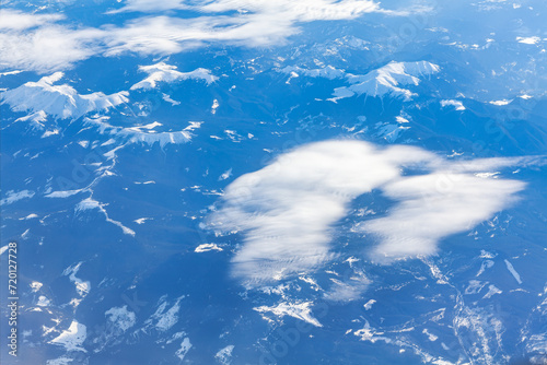 Clouds in the blue sky with snowy peaks as seen through window of an aircraft