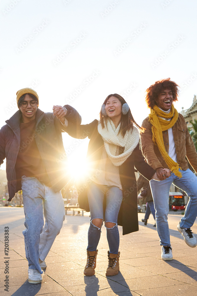 Naklejka premium Group of multiracial friends having fun outdoors, walking holding hands and laughing at the city during winter time.