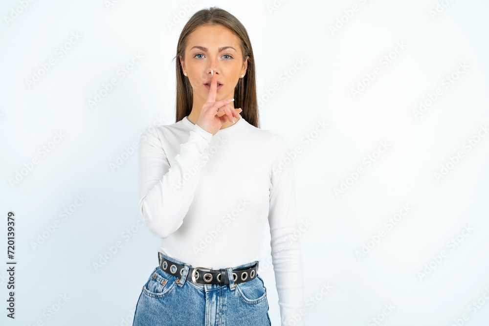 young beautiful caucasian woman wearing white long sleeve T-Shirt makes silence gesture, keeps finger over lips. Silence and secret concept. young beautiful caucasian woman wearing white long sleeve T-Shirt makes silence gesture, keeps finger over lips. Silence and secret concept.