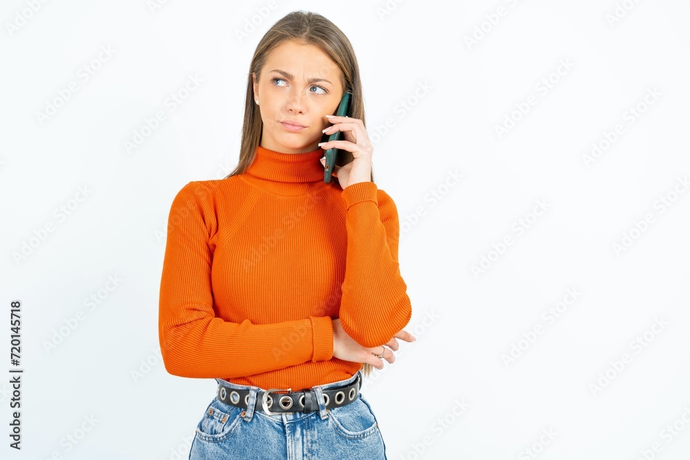 Sad young beautiful girl wearing orange turtleneck talking on smartphone. Communication concept. Sad young beautiful girl wearing orange turtleneck talking on smartphone. Communication concept.