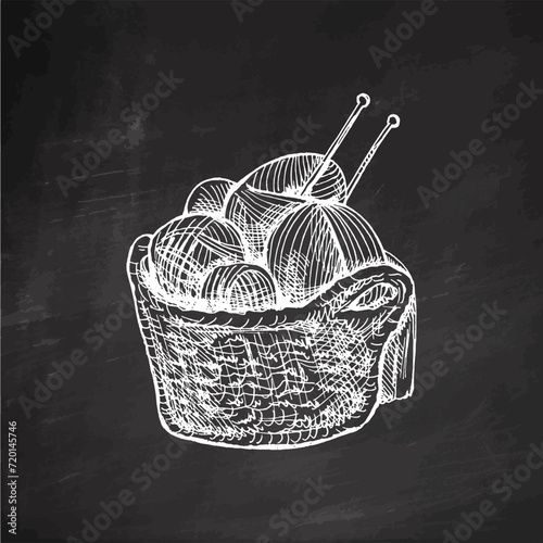 Hand-drawn sketch of basket with balls of yarn, wool and knitting needles on chalkboard background. Knitwear, handmade, knitting equipment concept in vintage doodle style. Engraving style. photo