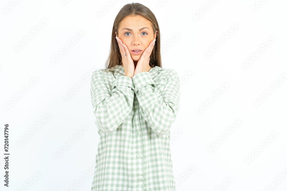 Upset Beautiful young woman wearing green plaid pyjama touching face with two hands Upset Beautiful young woman wearing green plaid pyjama touching face with two hands