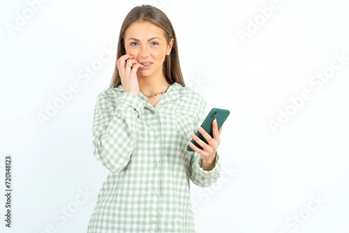 Afraid funny Beautiful young woman wearing green plaid pyjama holding telephone and bitting nails photo