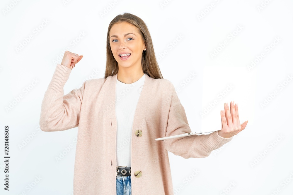 Obraz premium Young beautiful woman wearing pink cardigan hold computer open mouth rise fist
