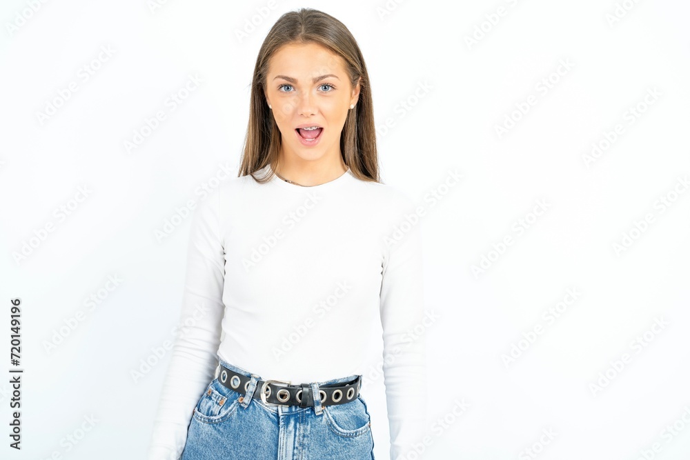 Obraz premium Oh my God. Surprised young beautiful girl wearing white T-shirt stares at camera with shocked expression exclaims with unexpectedness,