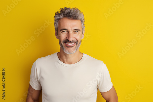 hombre español maduro de 50 años posando sonriente con una camiseta blanca, sobre fondo amarillo