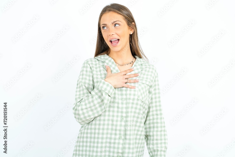 Joyful Young beautiful woman wearing green plaid pyjama expresses positive emotions recalls something funny keeps hand on chest and giggles happily. Joyful Young beautiful woman wearing green plaid pyjama expresses positive emotions recalls something funny keeps hand on chest and giggles happily.