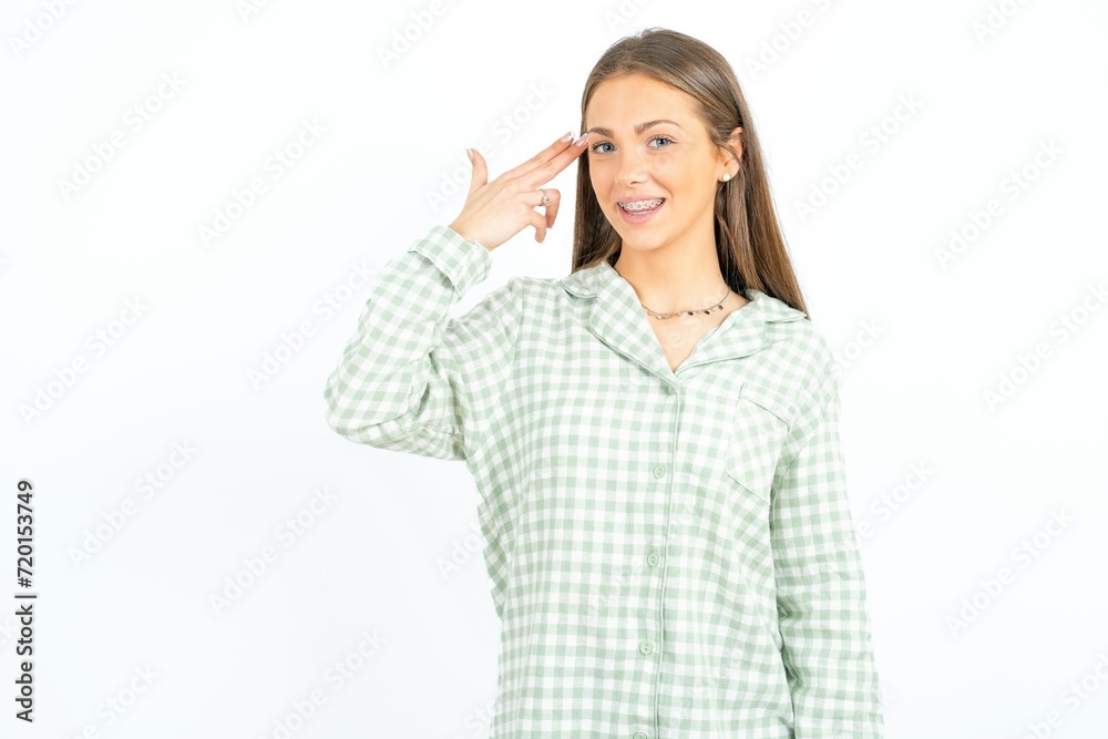 Young beautiful woman standing over white studio background foolishness around shoots in temple with fingers makes suicide gesture. Funny model makes finger gun pistol Young beautiful woman standing over white studio background foolishness around shoots in temple with fingers makes suicide gesture. Funny model makes finger gun pistol