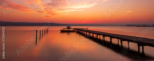 Scenic view of exciting red sunset at the shore with a wooden pier and moored boat