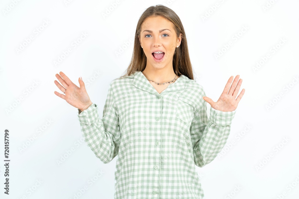 Delighted positive young beautiful woman wearing green plaid pyjama, opens mouth and arms palms up after having great result Delighted positive young beautiful woman wearing green plaid pyjama, opens mouth and arms palms up after having great result