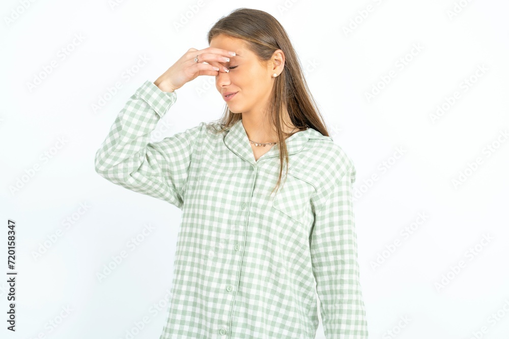 Sad young beautiful woman wearing green plaid pyjama, suffering from headache holding hand on her face Sad young beautiful woman wearing green plaid pyjama, suffering from headache holding hand on her face