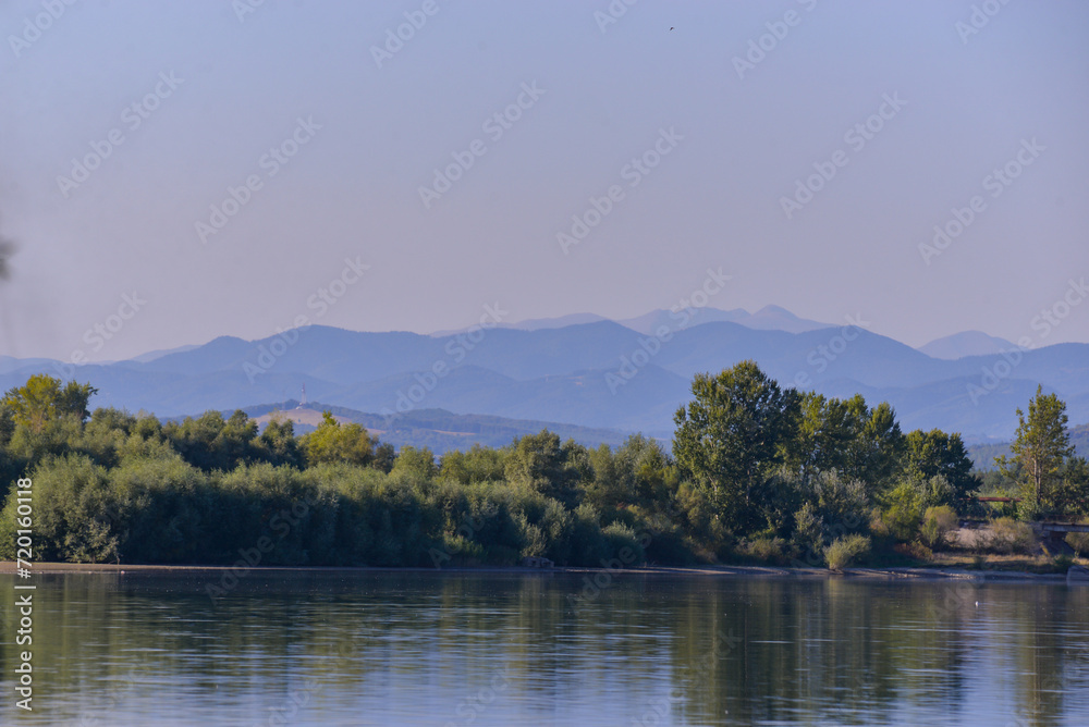 Summer landscape with a blue lake and mountains in the background. Green forest at the edge of the water at the foot of the Carpathians